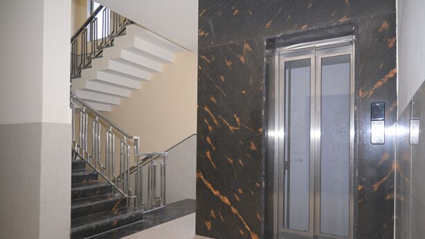 Un ascensore moderno con finiture metalliche, accanto a una scala con ringhiera in vetro.