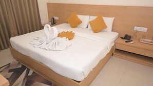 Camera d'albergo con un letto rifatto, un comodino con telefono e telecomandi, e una presa elettrica.
