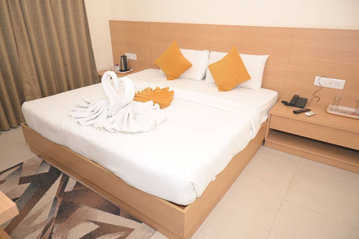 A hotel room with a bed, a nightstand, a telephone, and a tray with glasses and a snack.