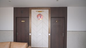 Una stanza con un'ampia porta in legno recante le scritte "OFFICE" e "02", un divano color beige e un muro decorato.