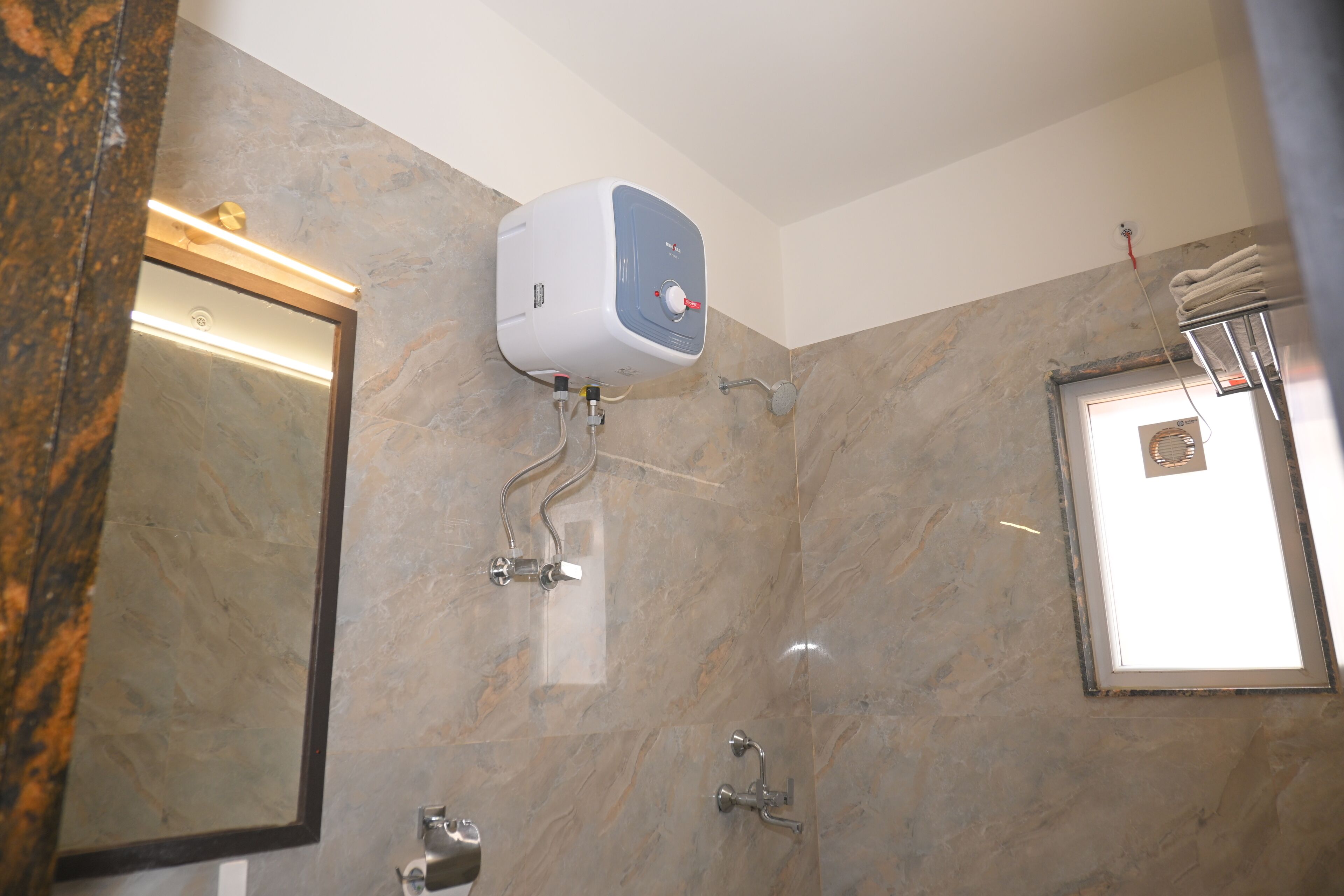 Un bagno con parete in marmo, asciugamani elettrico, porta asciugamani e doccia.