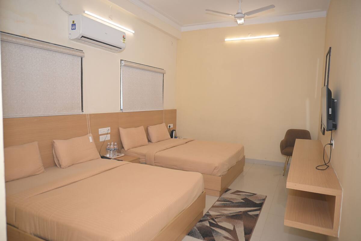 A hotel room with two beds, a desk, a chair, a television, and an air conditioning unit.