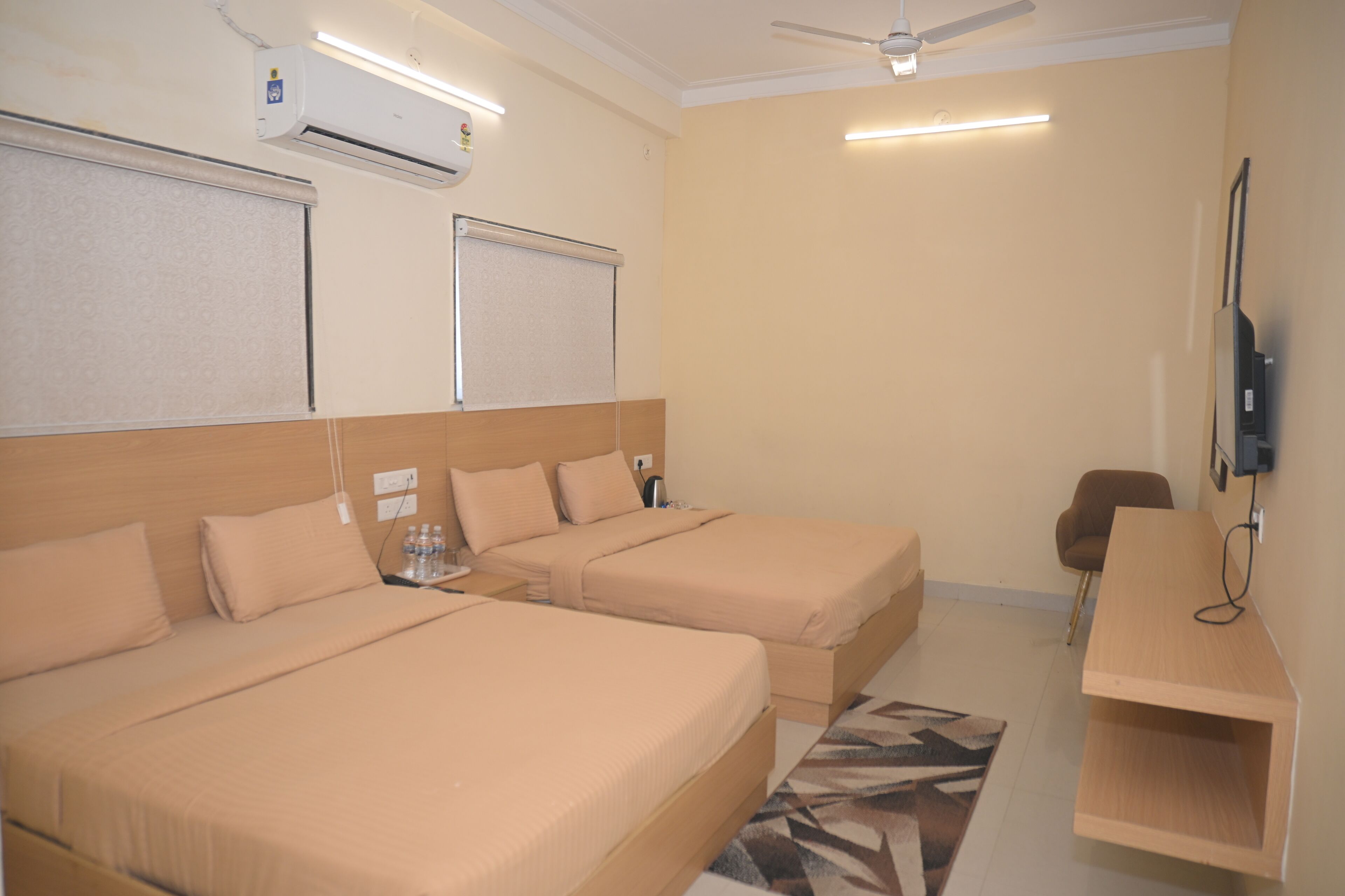A hotel room with two beds, a desk, a chair, a TV, and an air conditioning unit.
