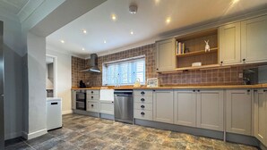 A modern kitchen with grey cabinets, a dishwasher, a built-in oven, and a window with blinds. - Hill House - UK49727 (King&rsquo;s Lynn)