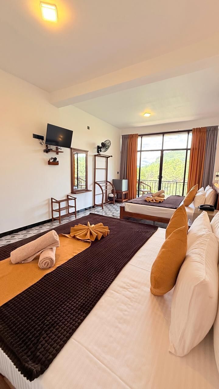 A hotel room with a large bed, a smaller bed, a desk with a chair, a television, and a balcony with curtains.