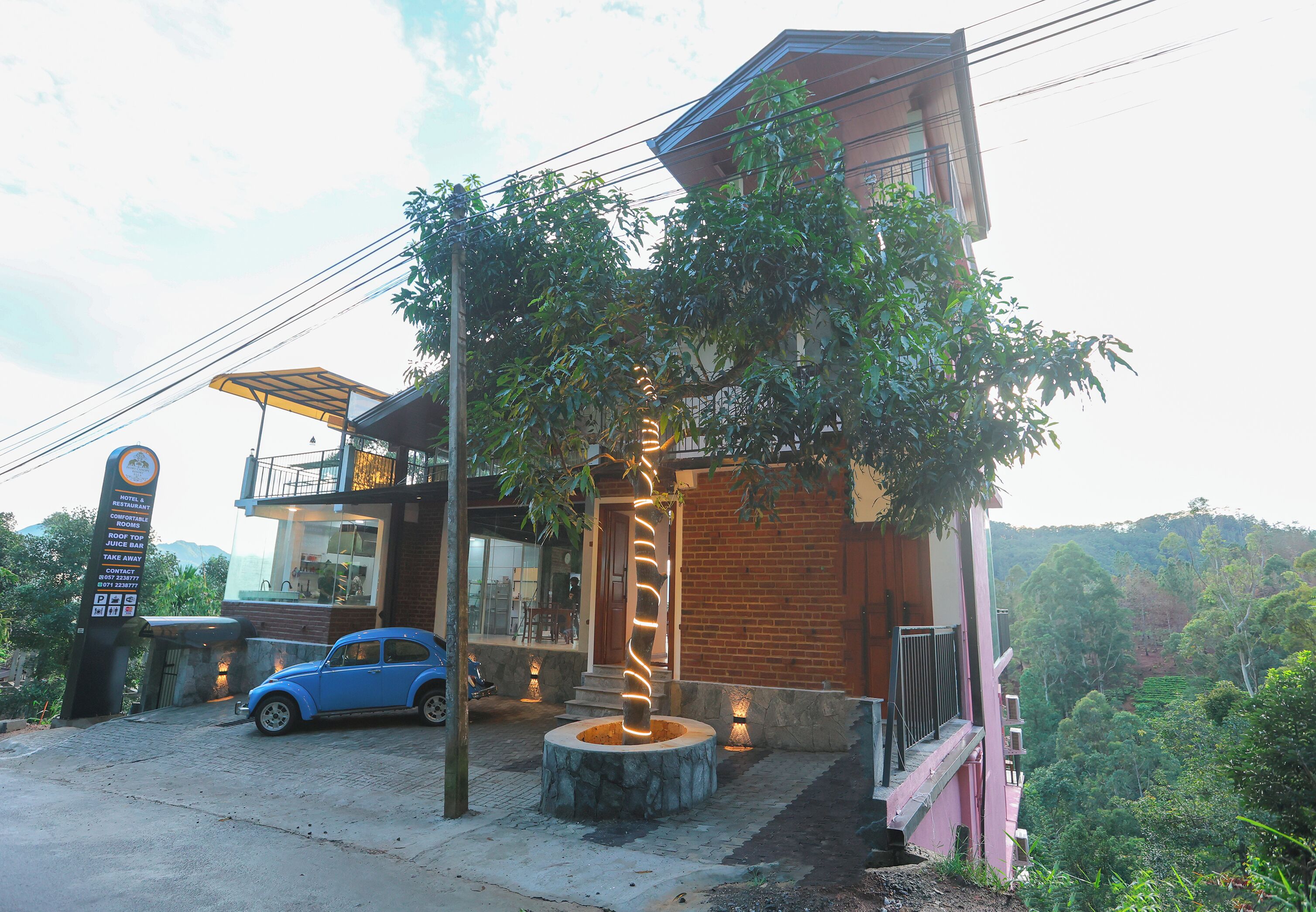 A modern building with a car parked in front, a tree with lights, and a sign indicating a restaurant and juice bar.