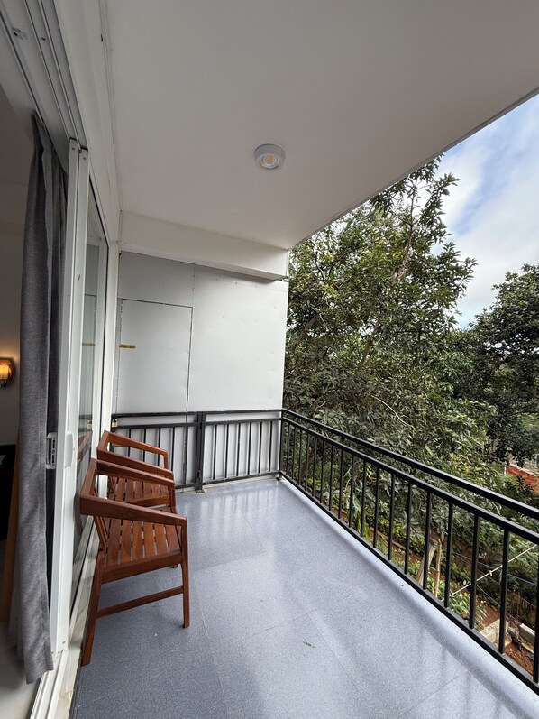 A balcony with a wooden chair, a white door, and a view of trees. - Ivory Canopy resort (Ella)