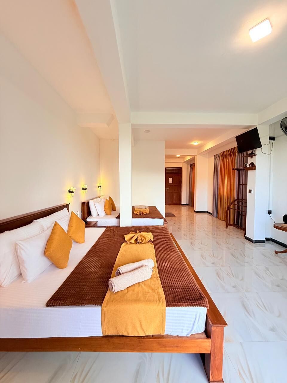 Habitació d'hotel amb un llit, un sofà i una taula petita plena de tovellons. Hi ha un passadís que condueix a una altra habitació.
