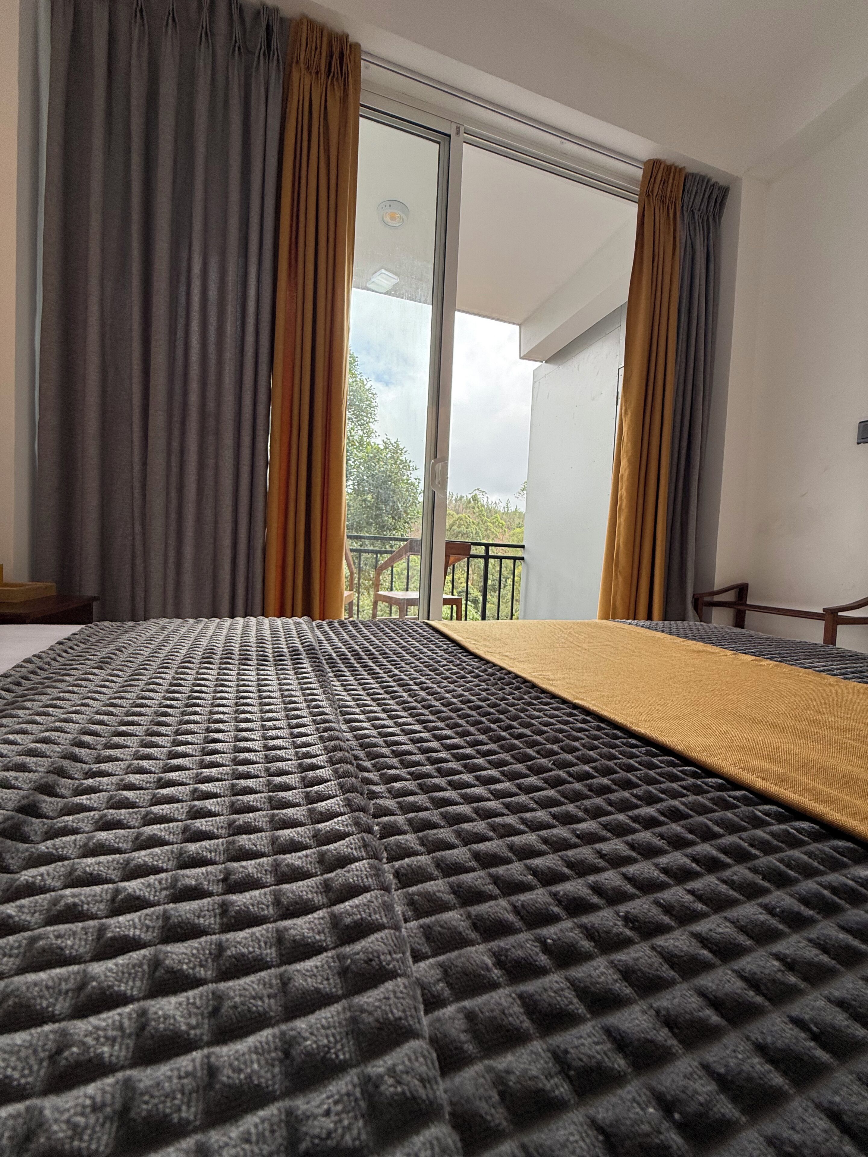 A bedroom with a large bed, sliding glass doors to a balcony, and a view of greenery outside.