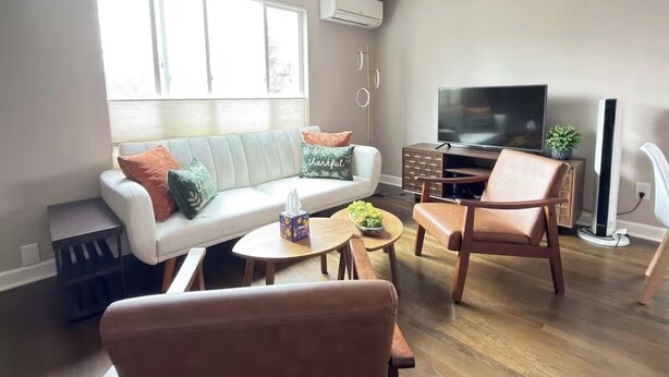 Ein Wohnzimmer mit einer Couch, zwei Sesseln, einem Couchtisch, einem Fernseher und einer kleinen Pflanze.