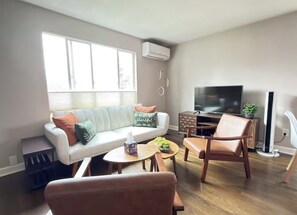 Una sala de estar con sofá, dos sillones, una mesa de centro, televisor y una planta pequeña.