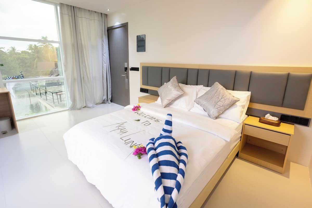 A hotel room with a large bed, a nightstand, a bedside table, a window with a view, and a balcony.
