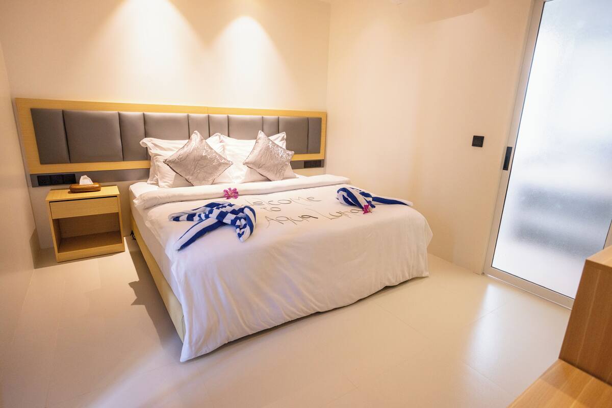 A modern hotel room with a large bed, a bedside table, and a wardrobe.