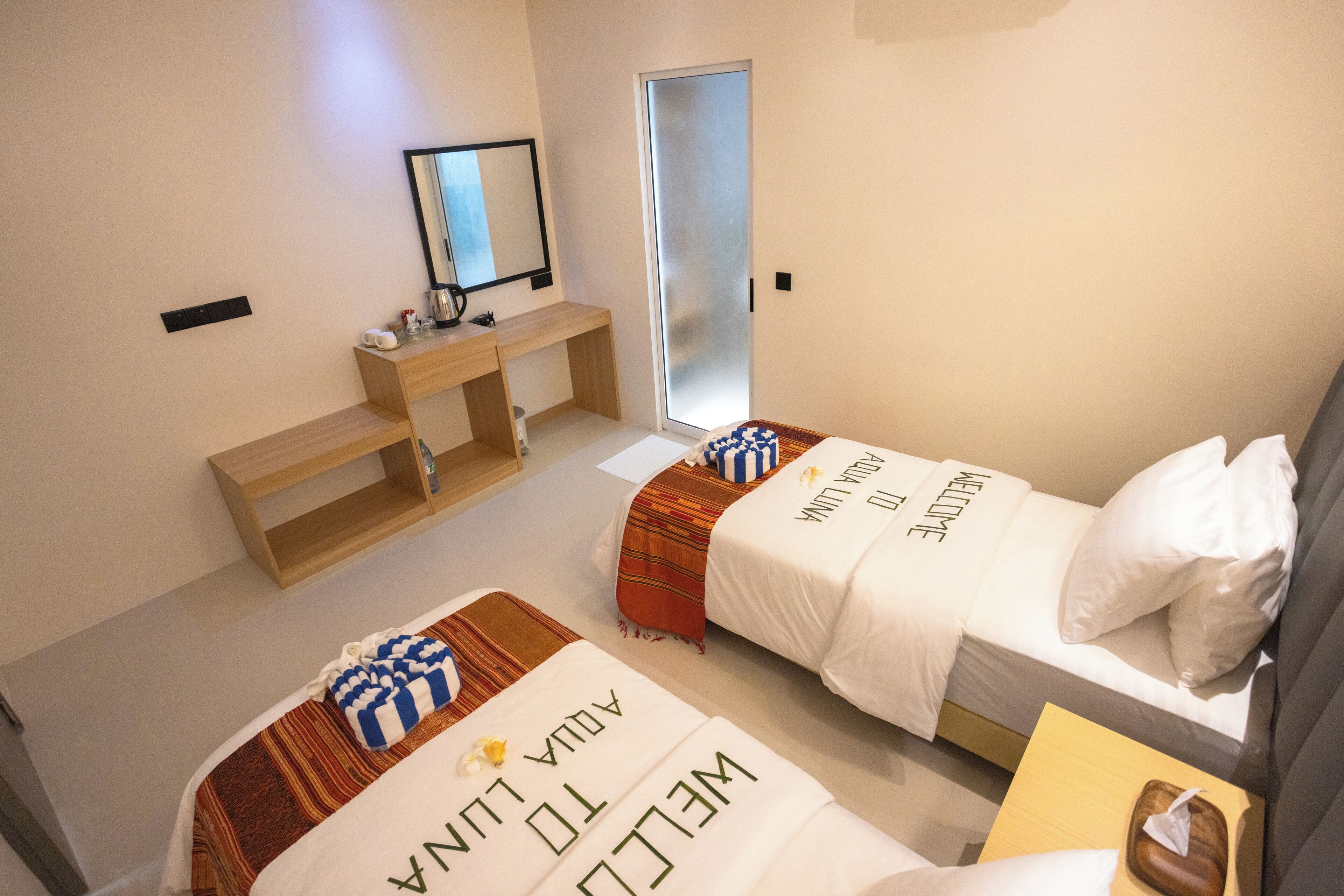 Habitación de hotel con dos camas, un escritorio, un espejo y una puerta.