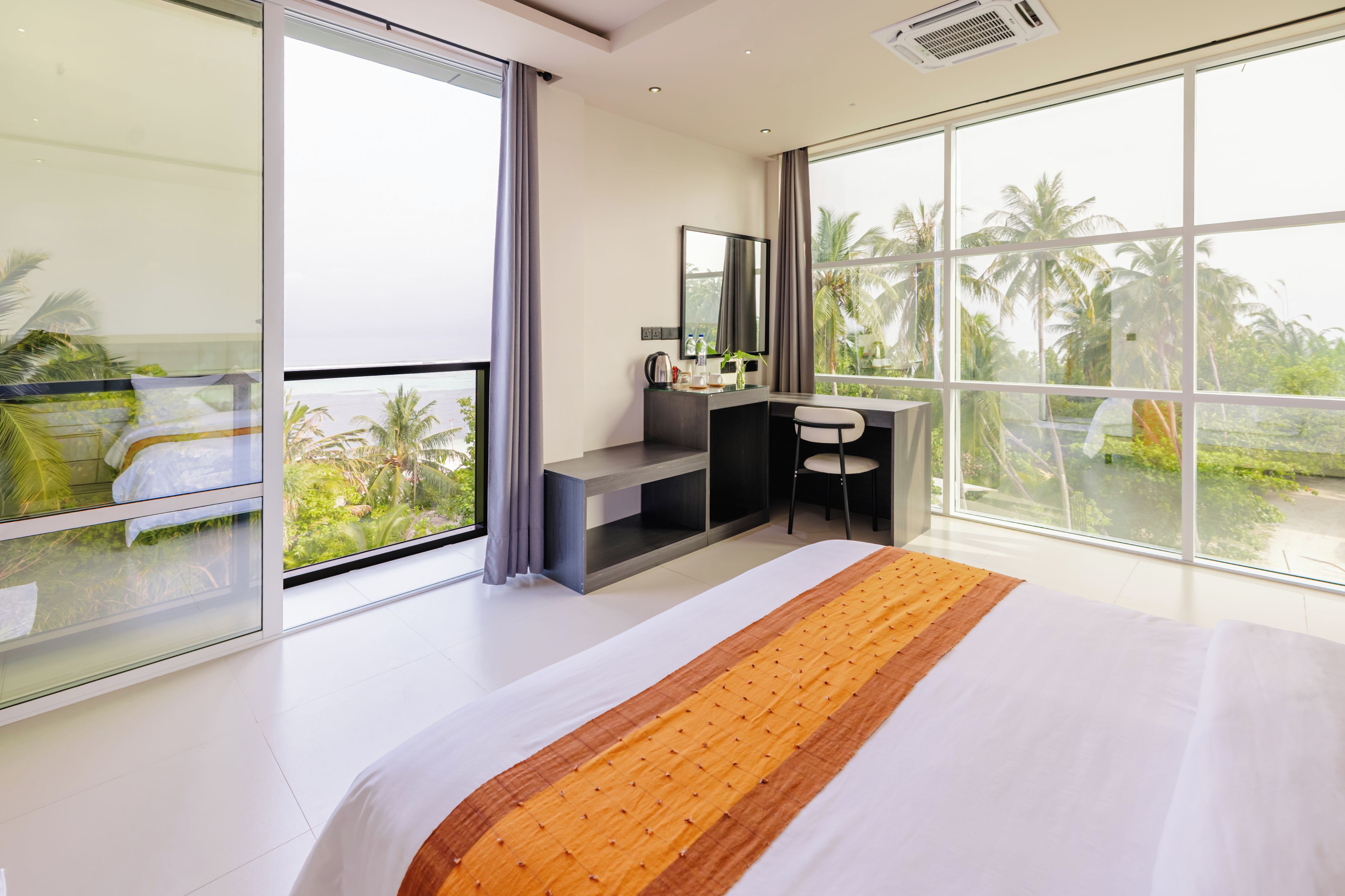 Habitación de hotel moderna con una cama grande, un escritorio y un balcón con vistas a palmeras.