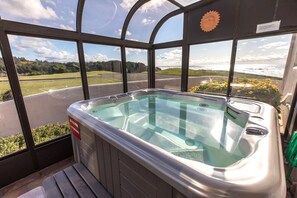 A hot tub with a glass enclosure, a sign indicating it is for adults only, and a view of the ocean and greenery.