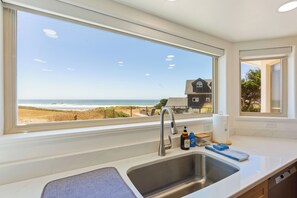 A kitchen with a large window overlooking a beach and a house.
