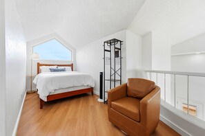 A bedroom with a bed, a standing heater, a brown leather chair, and a window.