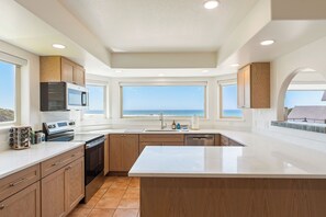 A modern kitchen with a large island, wooden cabinets, and a view of the ocean.