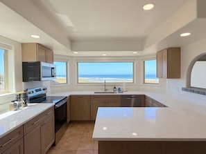 Una cocina moderna con una isla grande, electrodomésticos integrados y vistas al océano.
