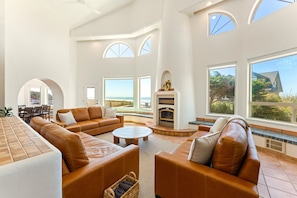 A spacious living room with a fireplace, leather sofas, and large windows offering views of the outdoors.