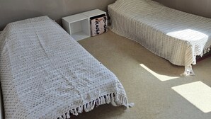 A small, dimly lit room with two single beds, a nightstand, and a storage box.