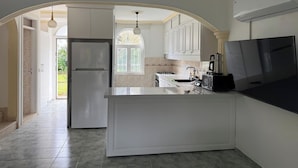 A modern kitchen with white cabinetry, a central island, a built-in oven, a refrigerator, a stove, and a large flat-screen TV. - Mete 3 Villa İçmeler Weekly Daily Rentals (Marmaris)
