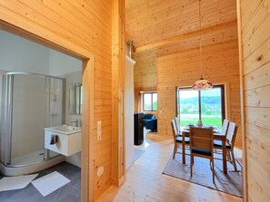 Ein Holzblockhaus-Interieur mit Dusche, einem Essbereich mit Tisch und Stühlen und einem großen Fenster mit Blick ins Freie.