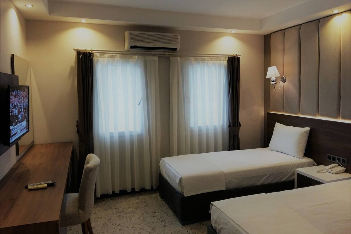 A hotel room with two beds, a desk, a TV, and an air conditioning unit.