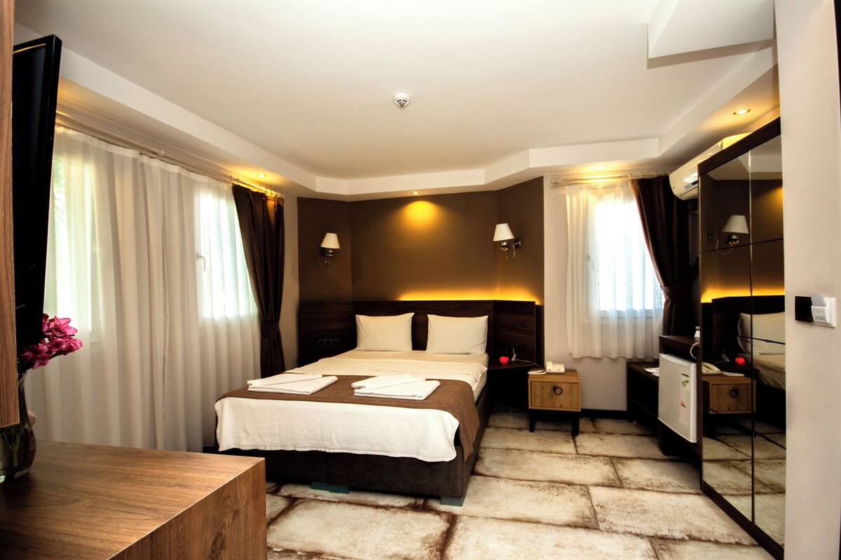 A hotel room with a large bed, a desk, a mirror, and a wardrobe.