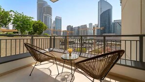 Un balcón con dos sillones de mimbre y una mesita, con vistas a un paisaje urbano con edificios modernos y una calle.