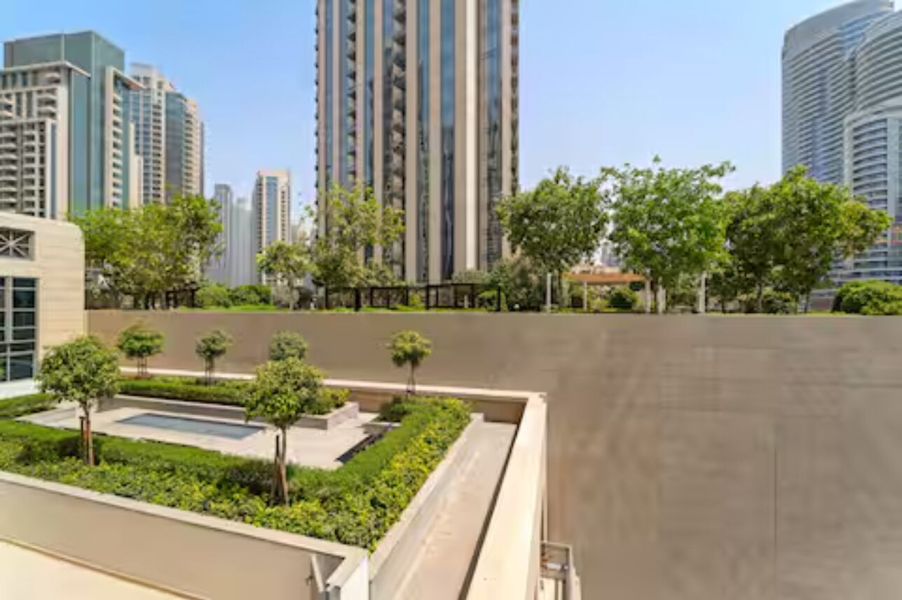 A modern urban residential area with high-rise buildings, a landscaped garden with trees, and a swimming pool.