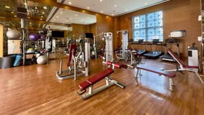 Un gimnasio amplio con diversos equipos de ejercicio, ventanas grandes y suelo de madera.