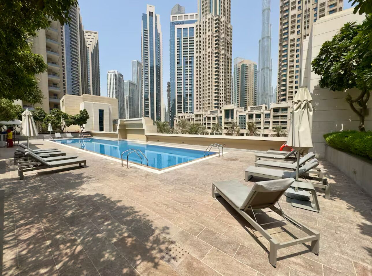 A rooftop pool area with lounge chairs and a swimming pool, surrounded by high-rise buildings.