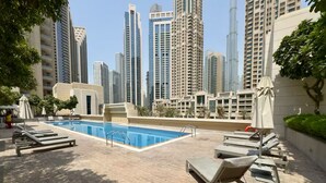 Un área de piscina en la azotea con sillones de descanso y una piscina, rodeada de edificios altos.