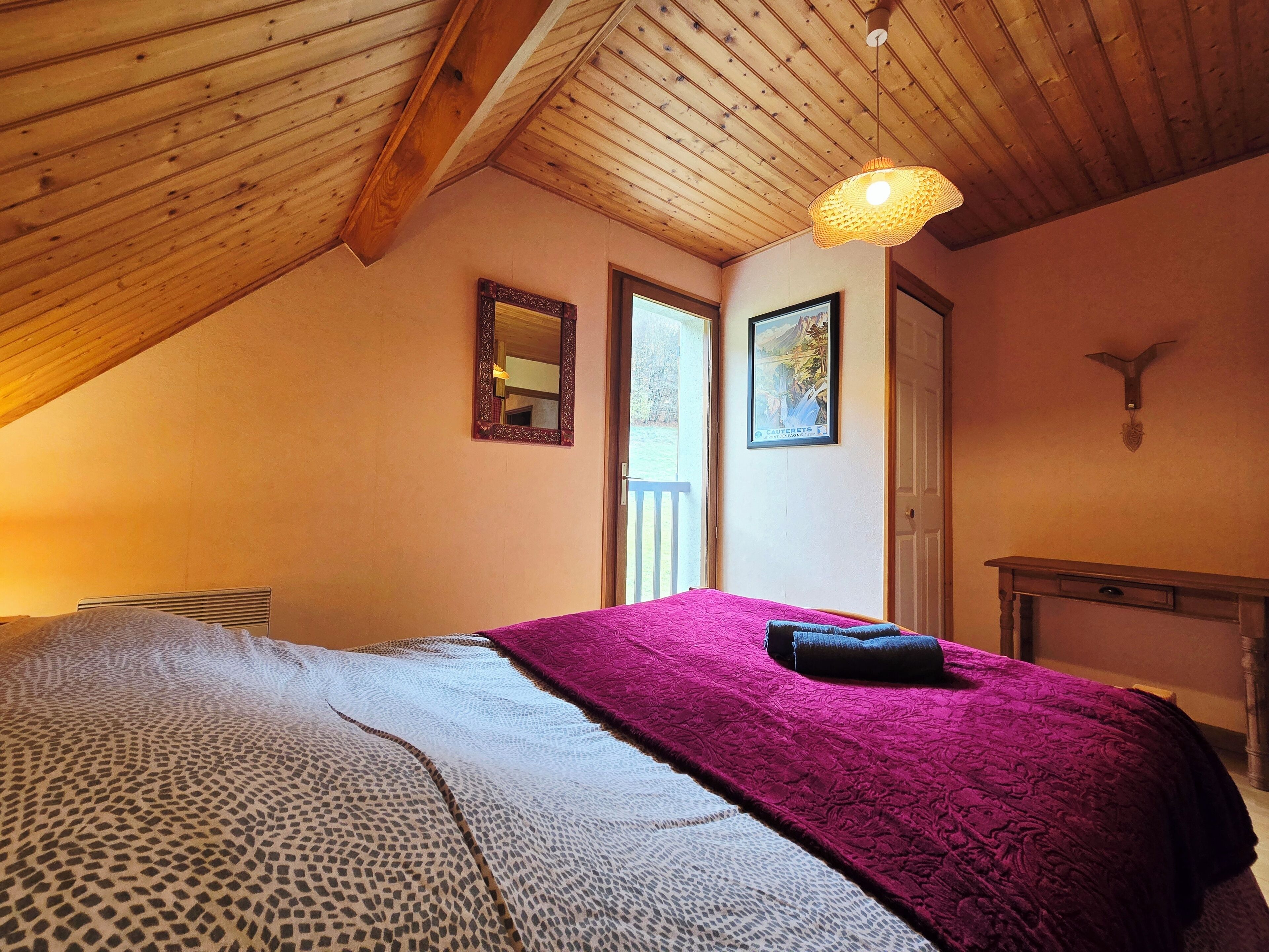 Quarto com teto inclinado, cama com colcha estampada, espelho e quadro na parede.