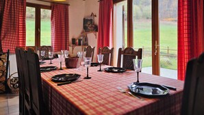 Un coin repas avec une nappe à carreaux, des chaises en bois et une grande fenêtre ornée de rideaux rouges.