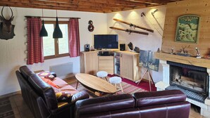 L’intérieur chaleureux d’un chalet avec un plafond en bois, une cheminée, un téléviseur et du matériel de ski accroché au mur.