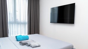 Hotellihuone, jossa on sänky, seinälle asennettu taulutelevisio ja ikkuna, jossa on verhot.