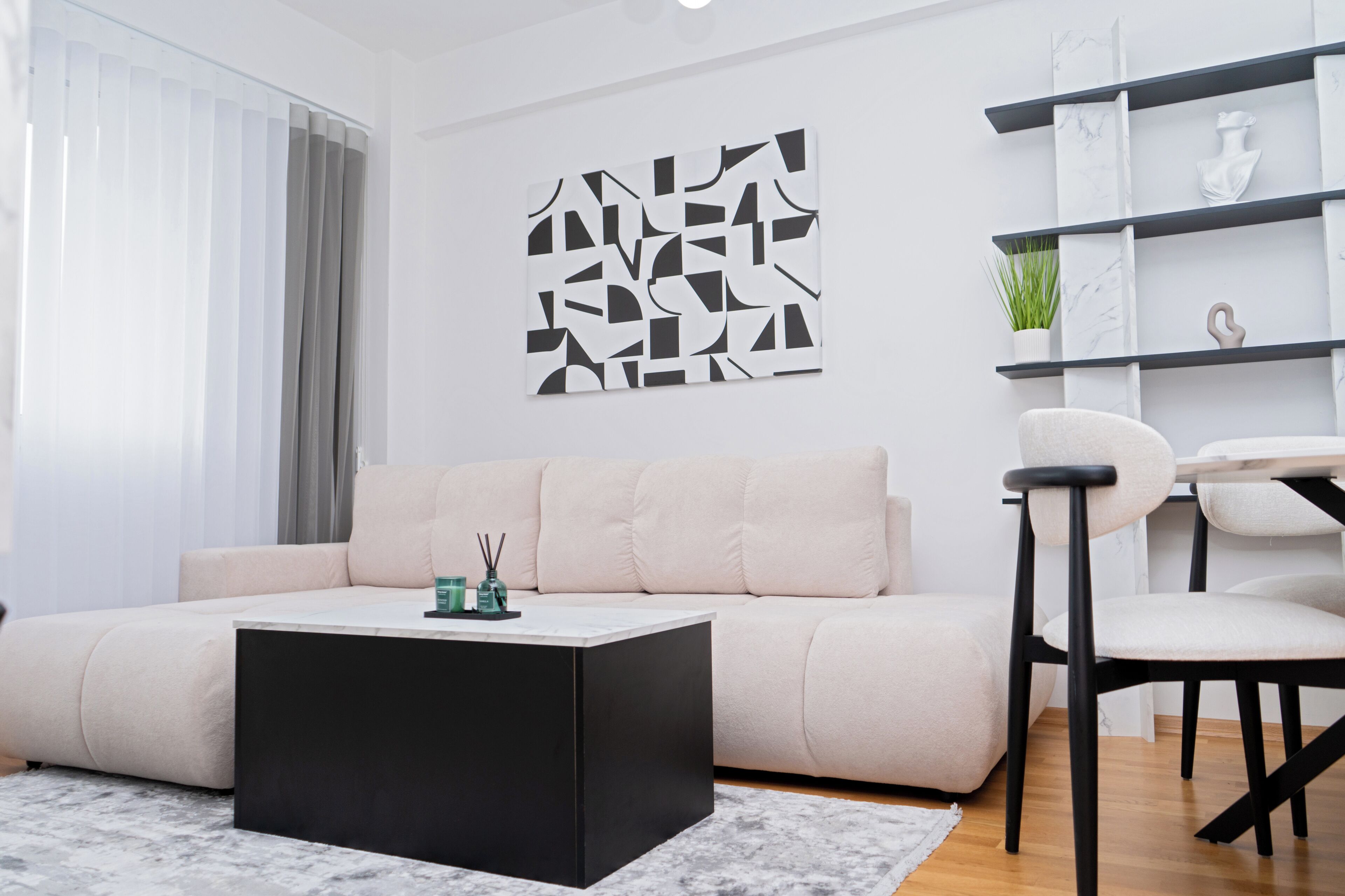 A modern living room with a beige sofa, a black coffee table, and a minimalist wall art piece.