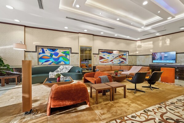 Un hall d’hôtel moderne avec un canapé, des fauteuils, une table basse, un téléviseur et des œuvres d’art accrochées aux murs.