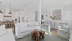 Una sala moderna con un sofá blanco, una mesa de centro de madera y una zona de comedor con barra.