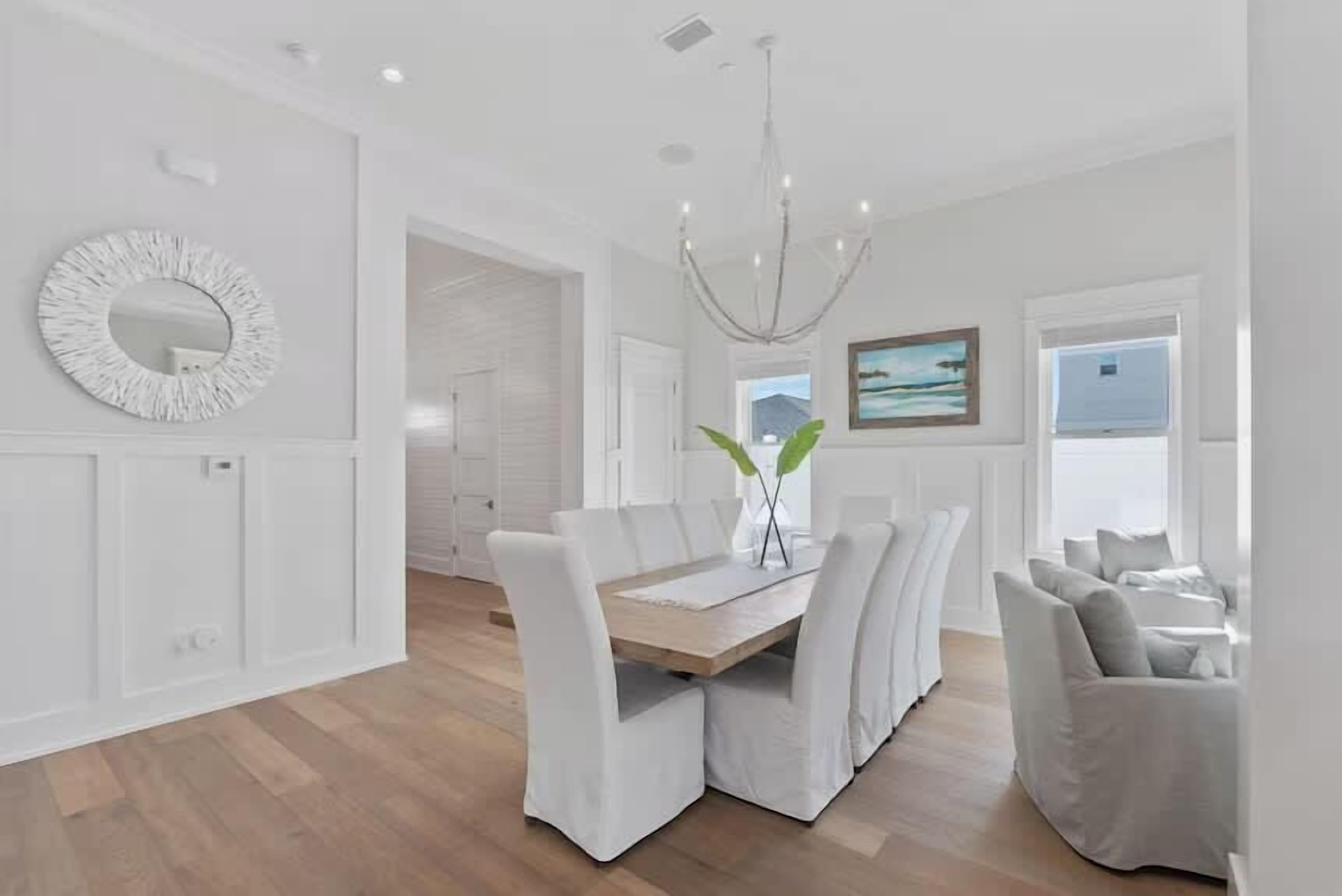 Een moderne eetruimte met een houten tafel en witte fauteuils, een kroonluchter en uitzicht op de omgeving.
