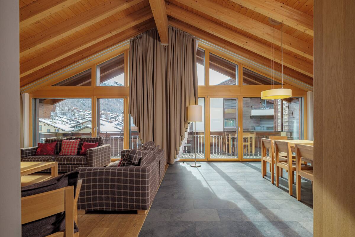 A spacious loft-style room with a high ceiling, large windows, a cozy seating area with a sofa and chairs, and a dining table.