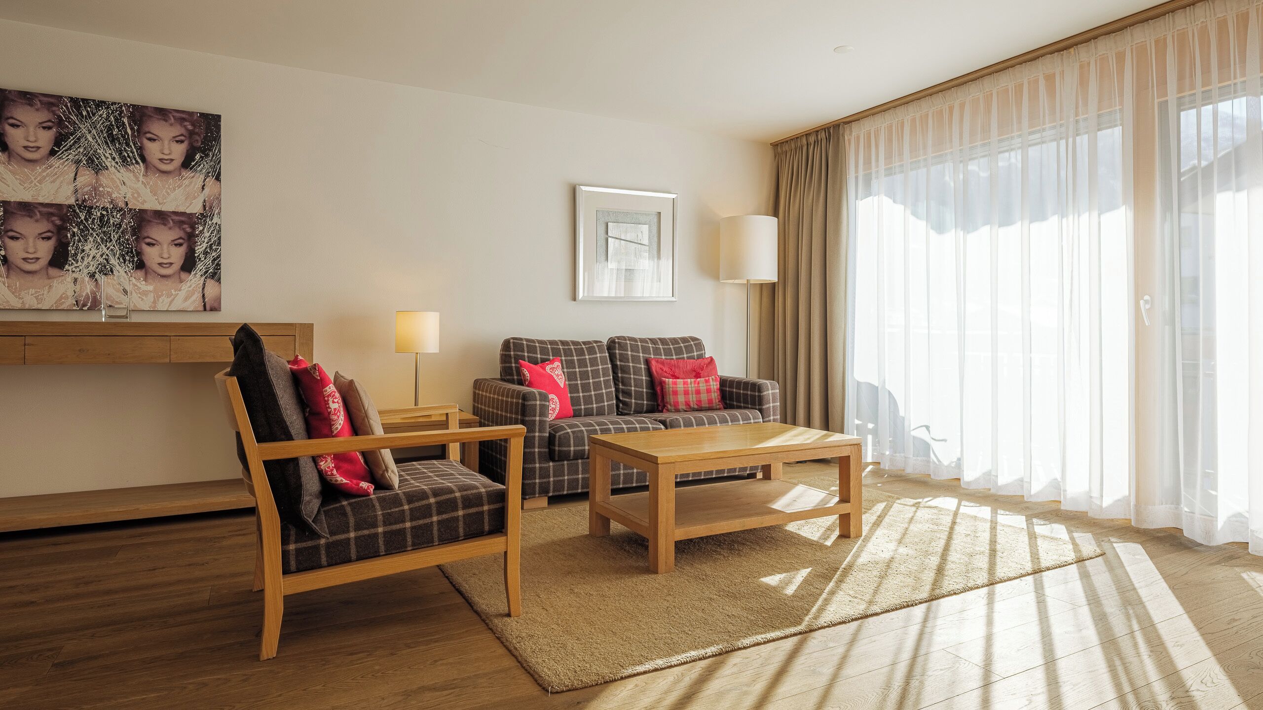 A modern living room with a sofa, armchair, and coffee table. There is a painting on the wall and a lamp beside the sofa.