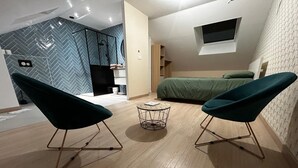 A modern room with two teal chairs facing a small round table, a bed with a green bedspread, and a herringbone-patterned wall. - To the hillside butterfly (Magenta)