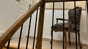 A staircase with a wooden handrail and black balusters, leading to a landing with a skylight. A patterned chair is placed on the landing. - To the hillside butterfly (Magenta)