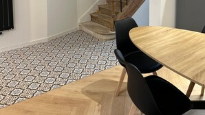 A dining area with a wooden table and black chairs, a patterned floor, and a staircase with wooden railings. - To the hillside butterfly (Magenta)