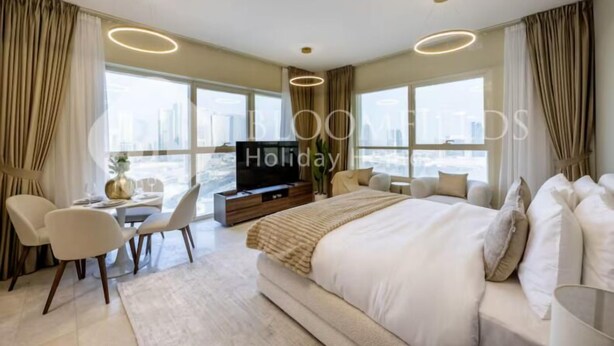 Ein modernes Hotelzimmer mit einem großen Bett, einem Fernseher, einem Essbereich und großen Fenstern mit Blick auf die Stadt.