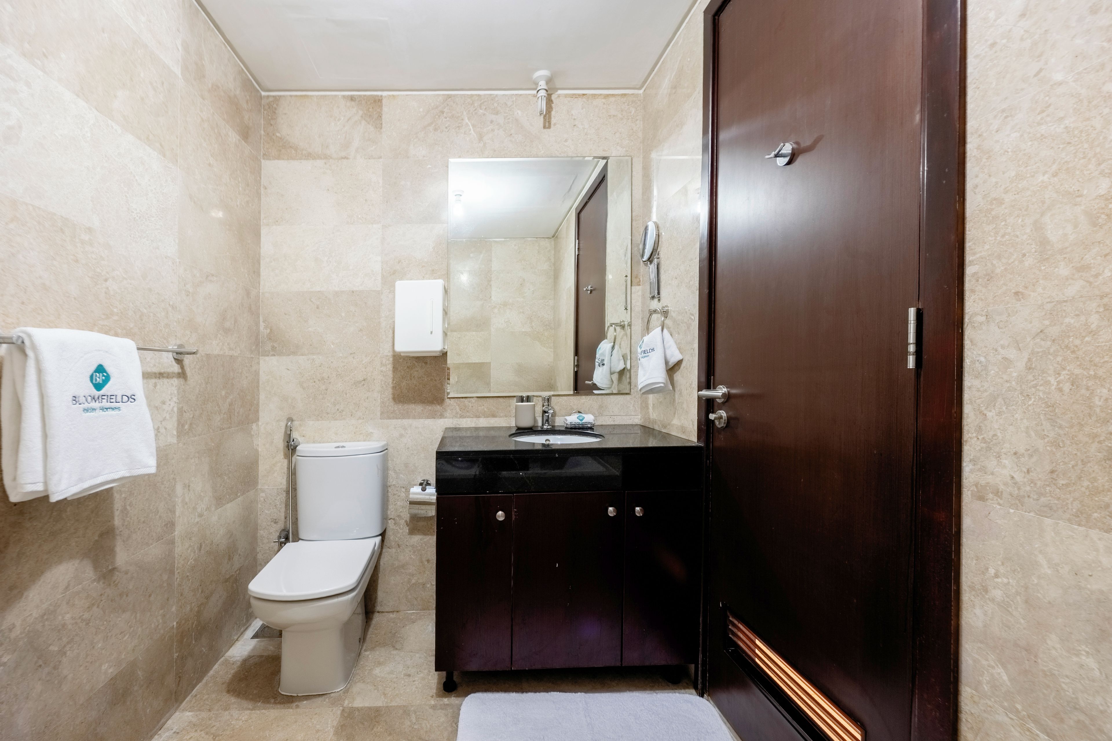 A bathroom with a toilet, sink, mirror, and towel rack.